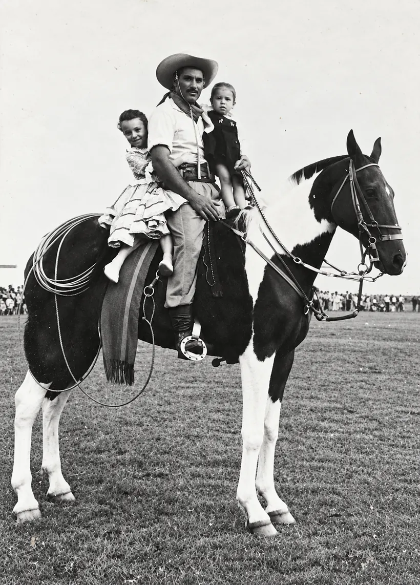 Fotografia antiga em preto e branco de um cavaleiro com duas crianças sobre um cavalo malhado